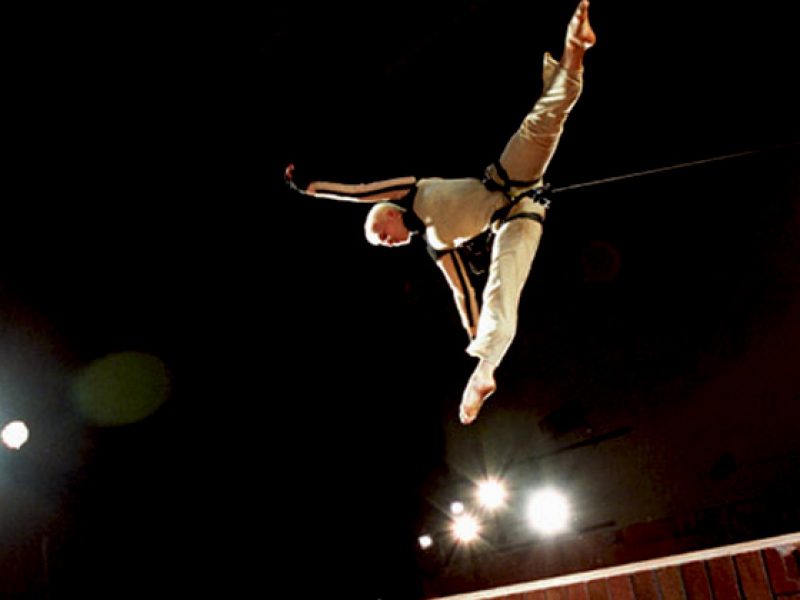 A vertical dance performer is mid flight, limbs extended in all directions. Taken from above, the action curiously defies gravity
