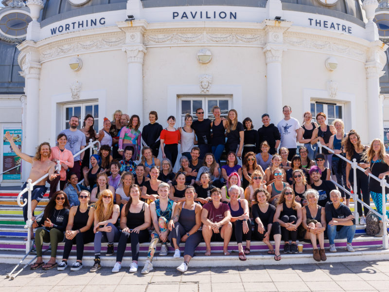 Festival crew and participants gather, sitting and standing on brightly painted steps in front of the pavilion theatre.
